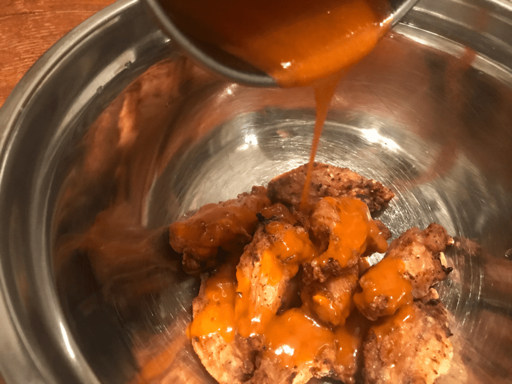 buffalo sauce being poured over air fried chicken wings
