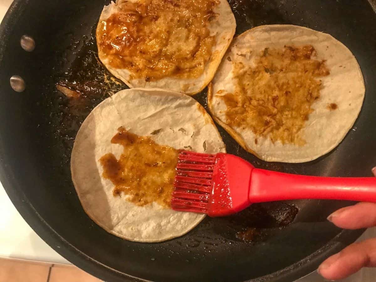 brushing consome on corn tortillas in skillet