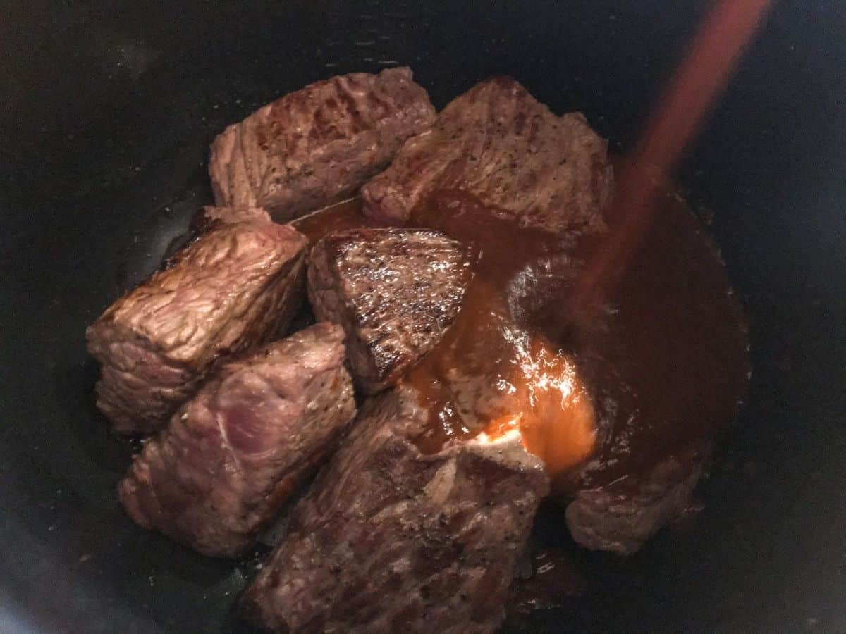 Pouring birria puree over seared chunks of chuck roast in instant pot