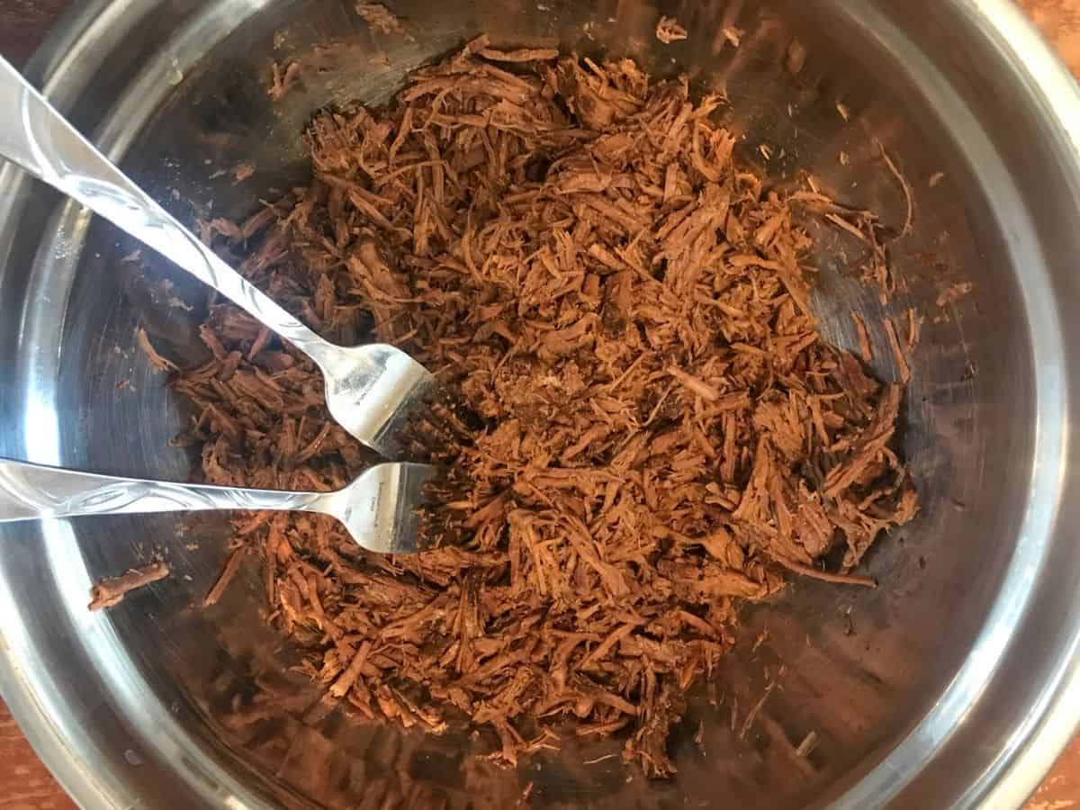 shredded chuck roast in a mixing bowl with 2 forks