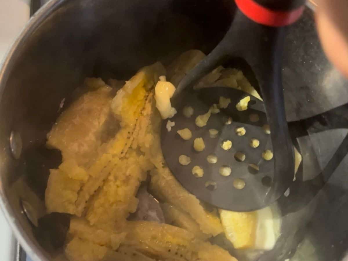 mashing cooked plantains in a pot with butter