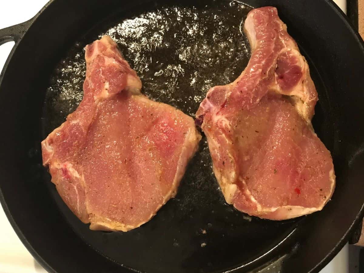 marinated pork chops cooking in a cast iron skillet