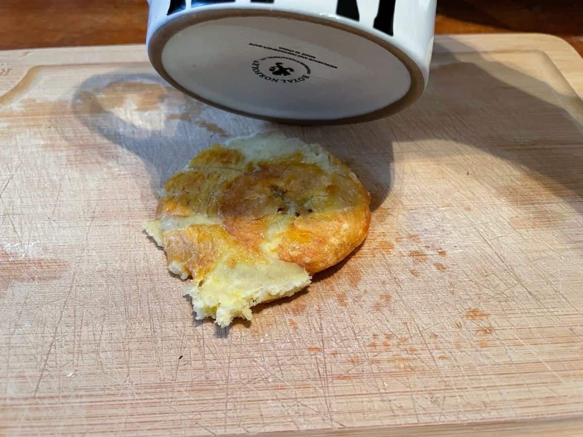 flattening a fried plantain with bottom of mug