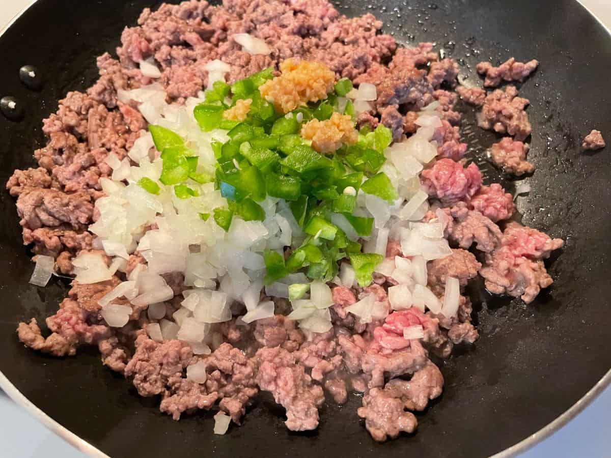 ground beef cooking with onion, jalapeño, and garlic in frying pan
