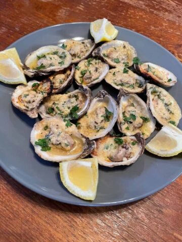 charbroiled oysters served on a blue plate with lemon wedges