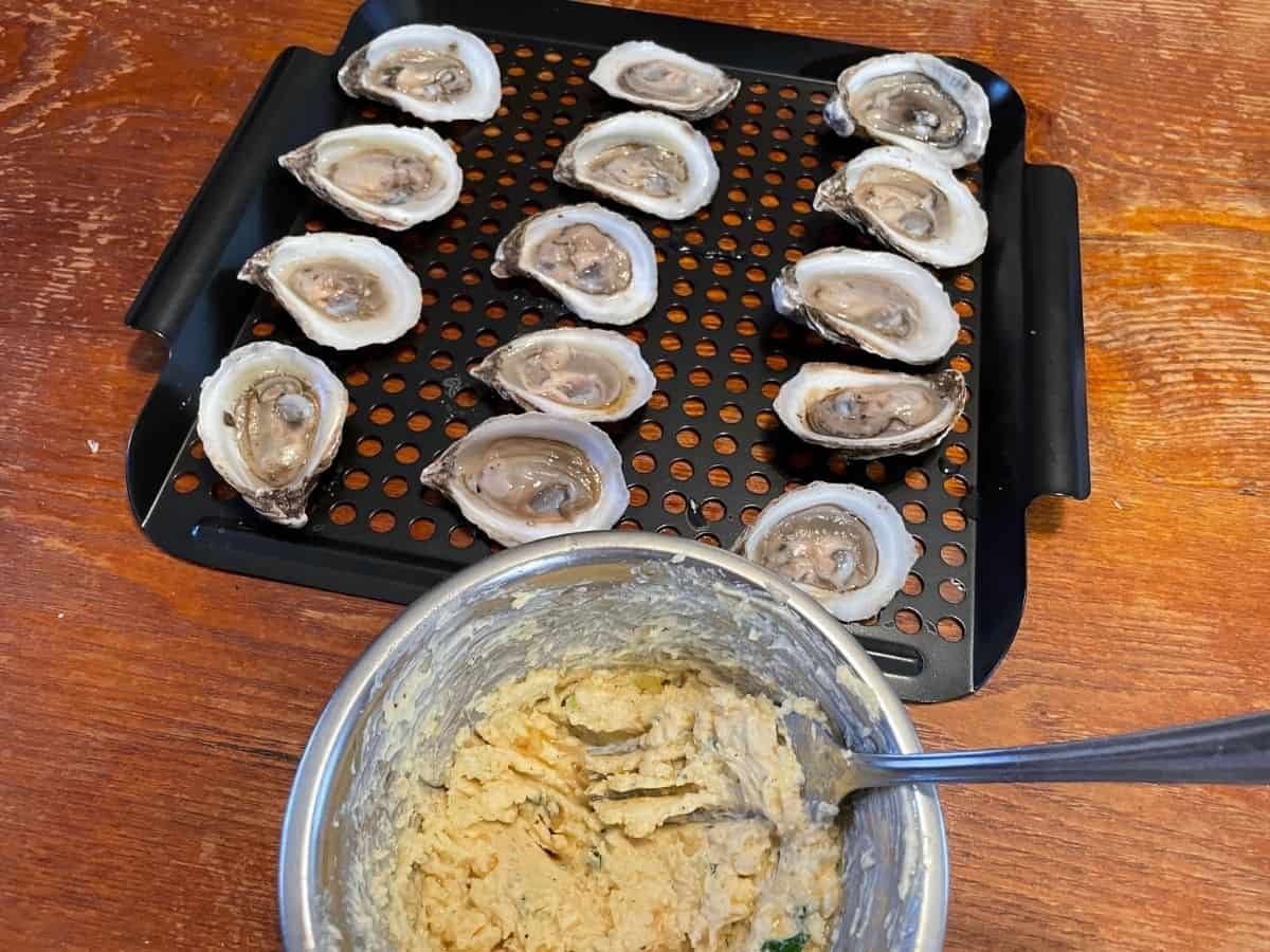 shucked oysters on a grill tray with bowl of garlic butter in front