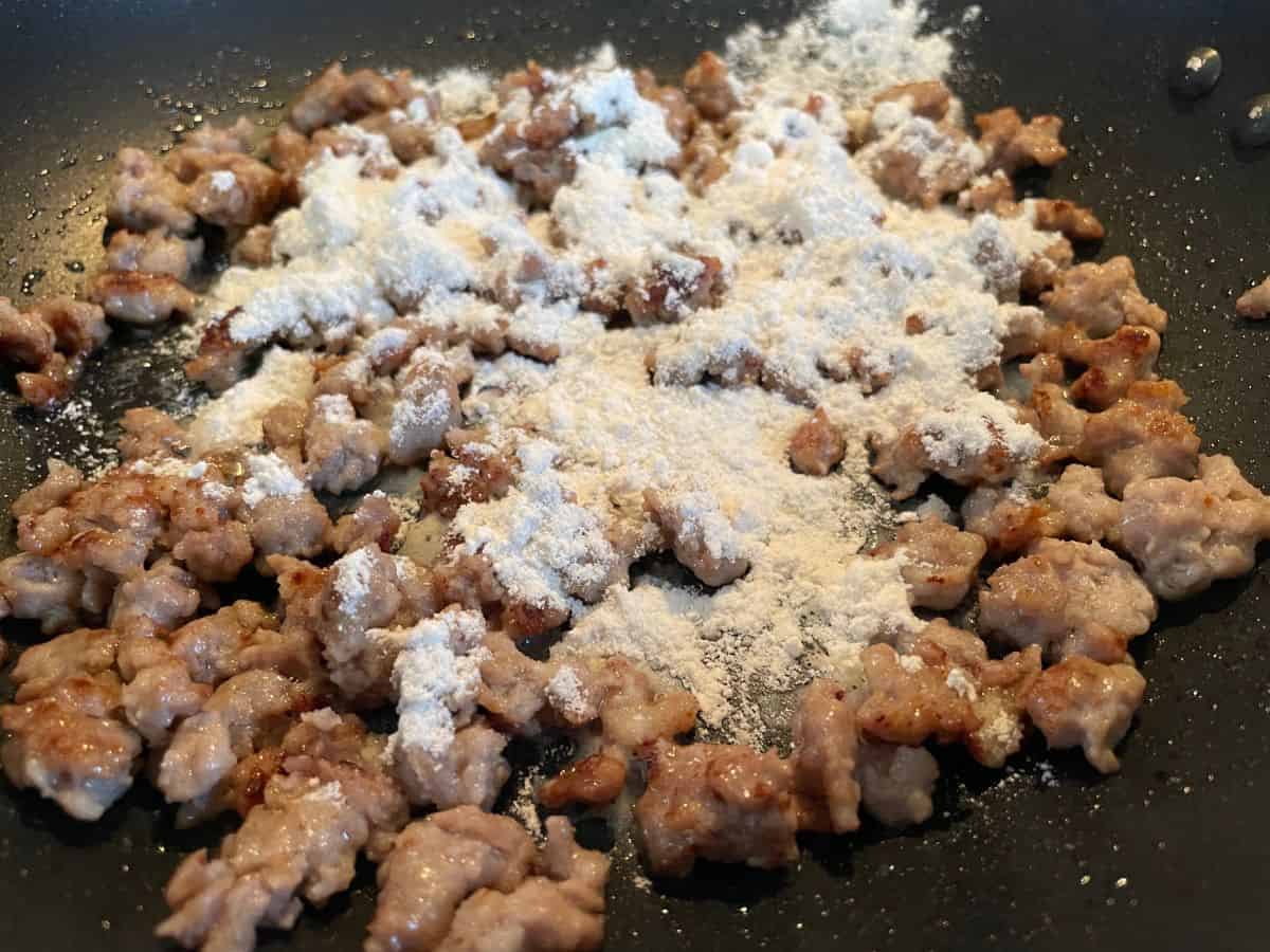 cooked crumbled sausage in pan with floured sprinkled on top