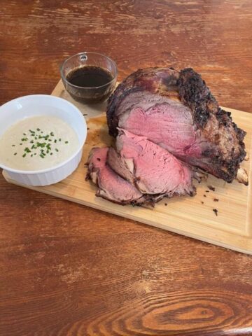 sliced prime rib on cutting board with bowl of horseradish cream and au jus