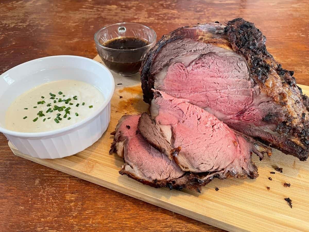 prime rib sliced on a cutting board with bowls of horseradish cream and au jus
