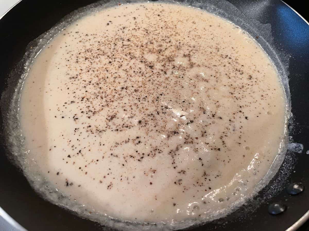 white gravy cooking in skillet with black pepper on top