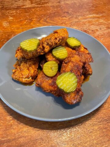 Nashville hot chicken tenders served with pickle chips on top of blue plate