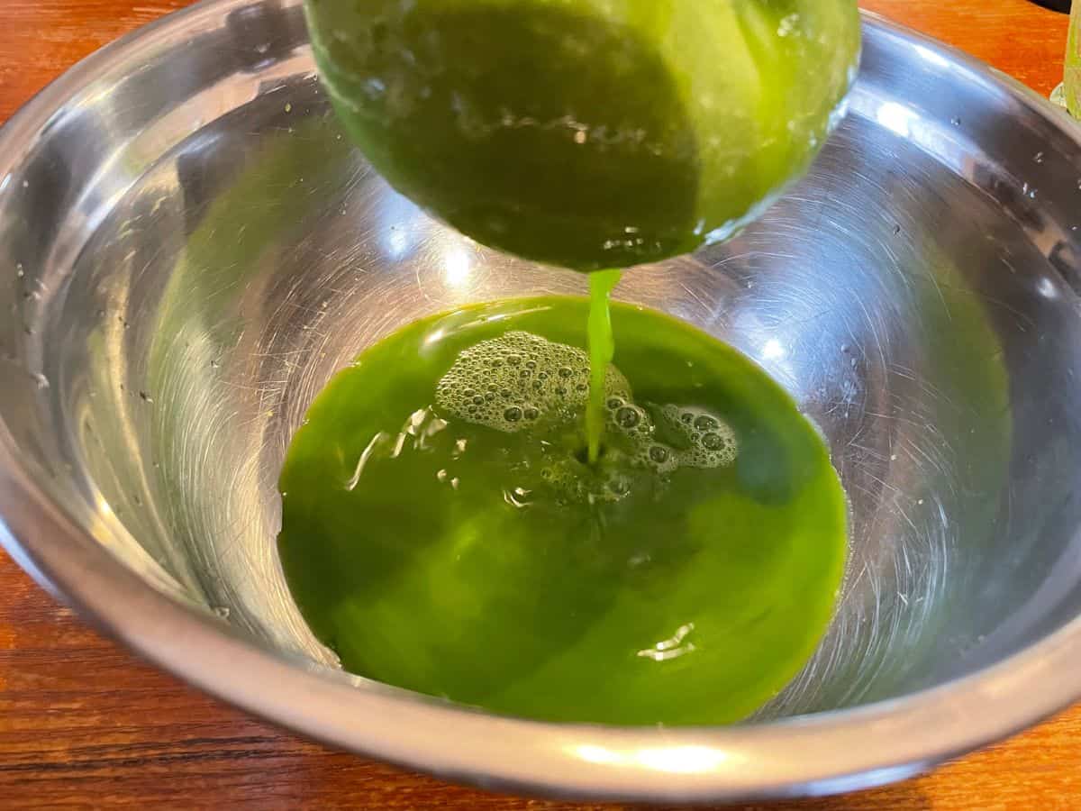 straining green juice through cheese cloth over bowl