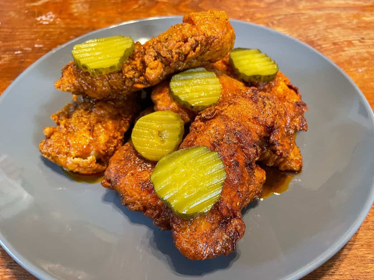 close up of hot chicken tenders with pickle chips on a blue plate