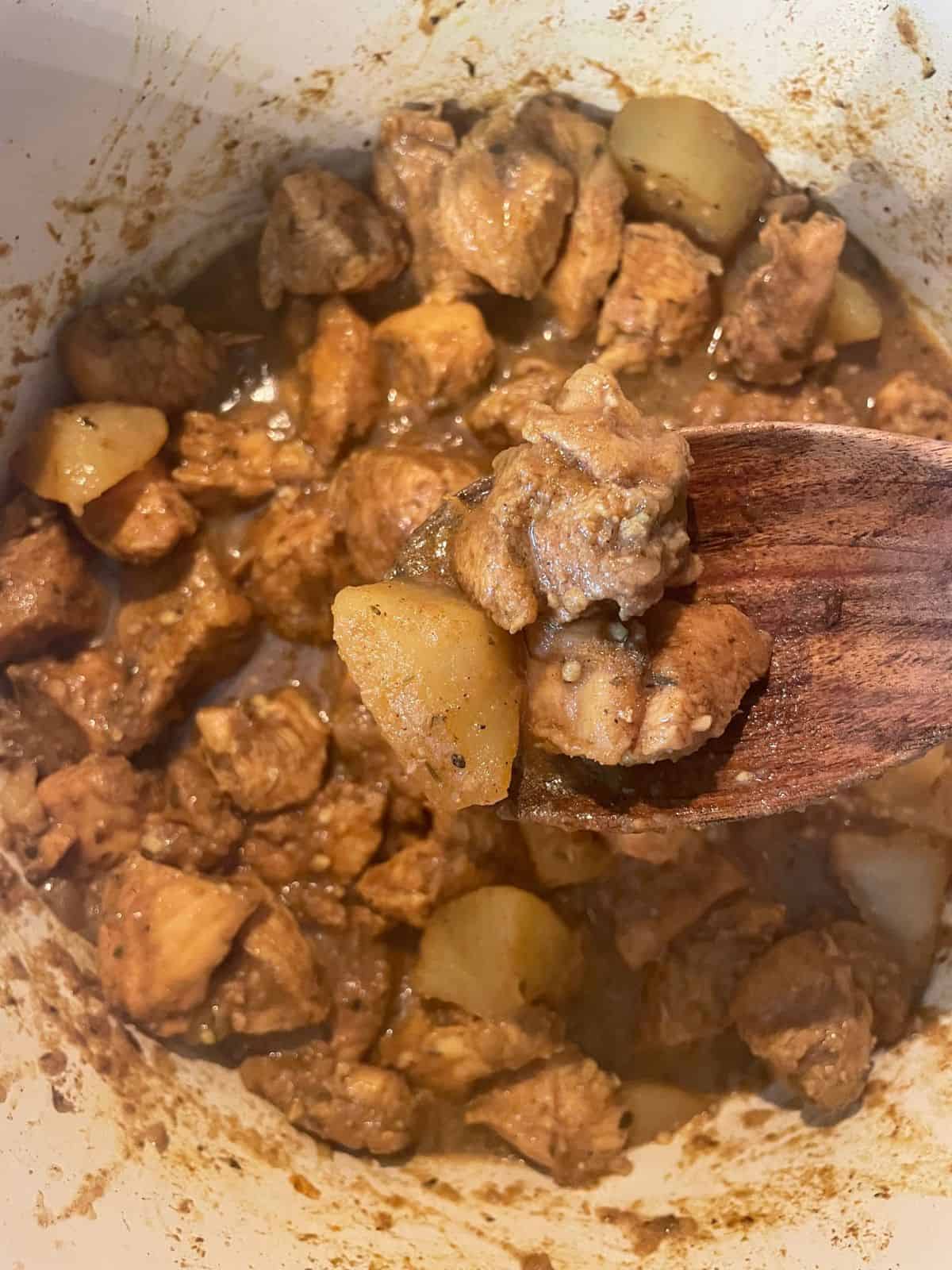 close up of curry chicken on a wooden spoon over pot