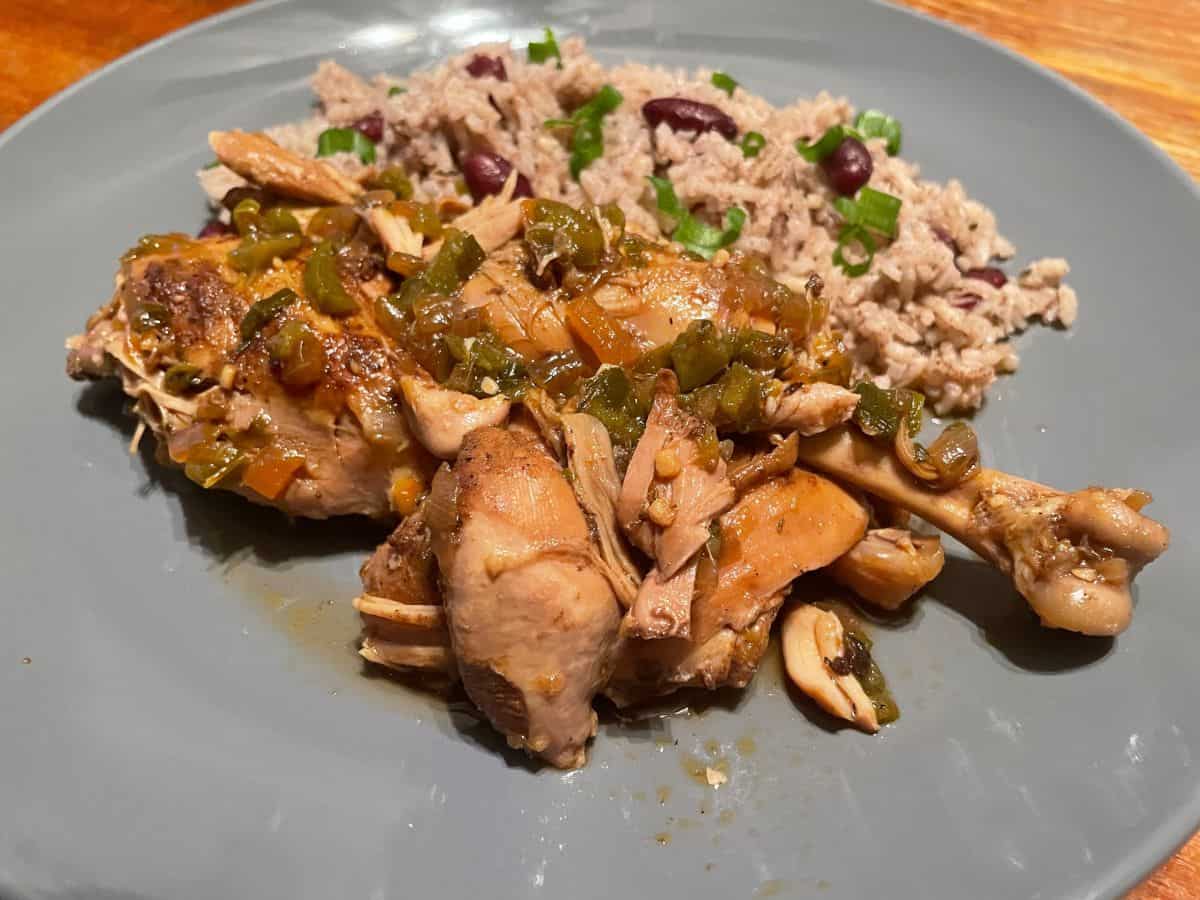 close up of served brown stew chicken with rice and peas