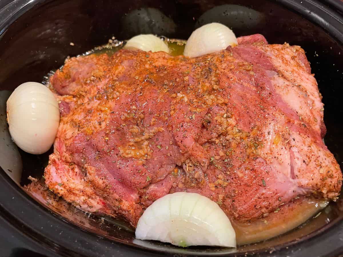 seasoned pork shoulder in slow cooker with onions and liquids