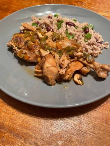 brown stew chicken served with rice and peas on a blue plate
