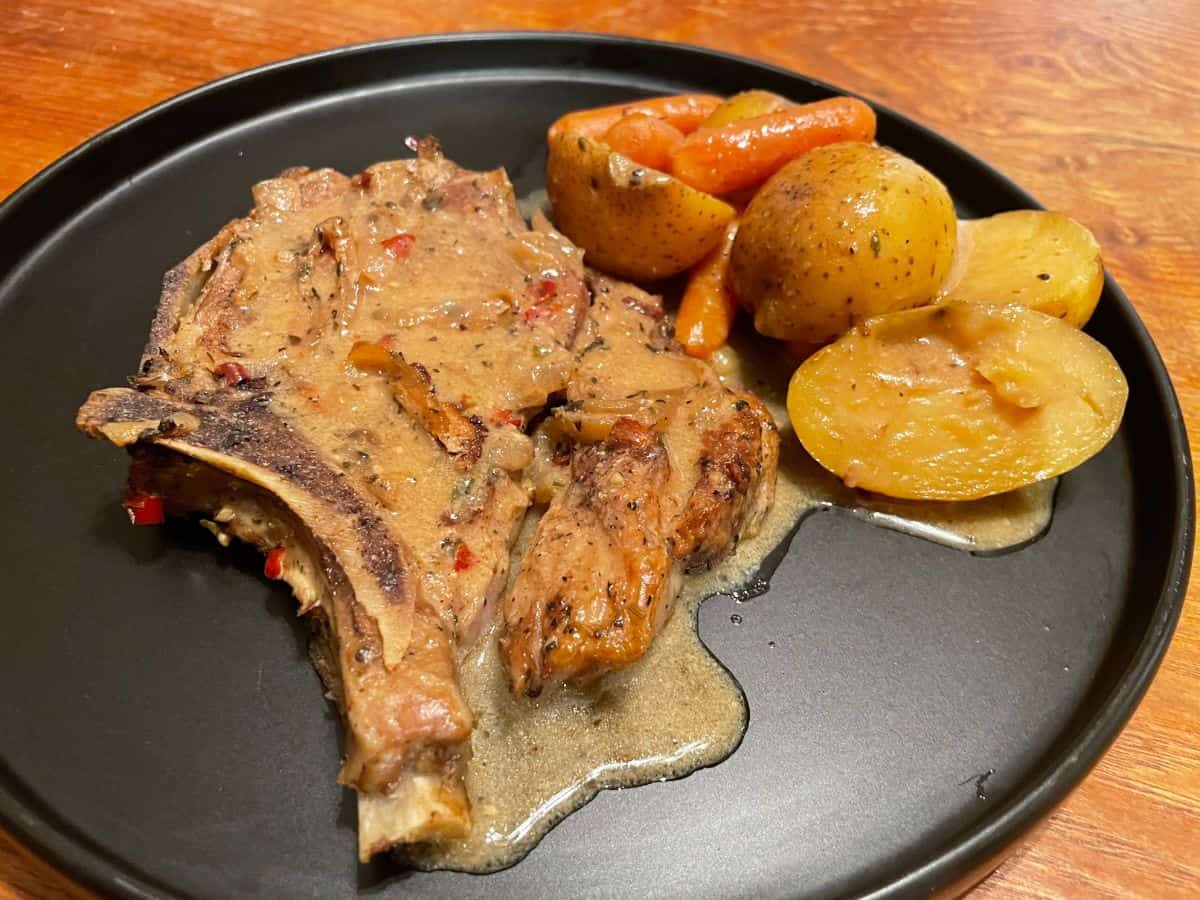 close up of smothers pork chops with vegetables served on a black plate