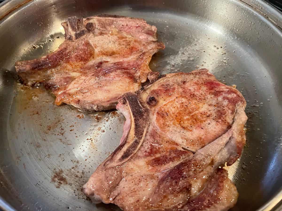 pork chops searing in a large stainless steel skillet