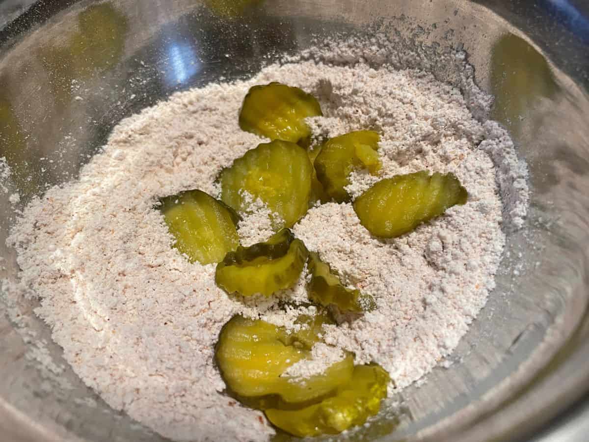 mixing bowl with pickle slices in seasoned flour.