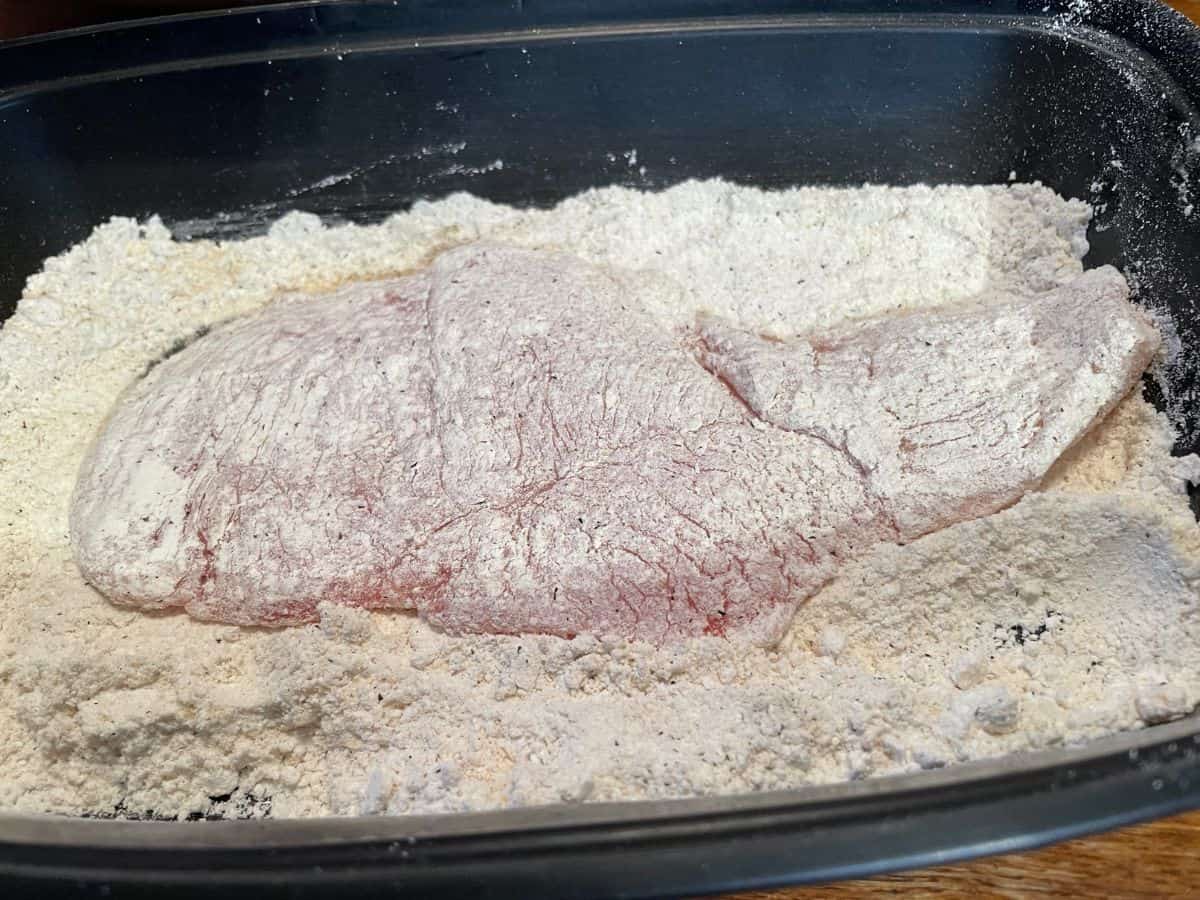 chicken breast coated in seasoned flour in shallow black bowl