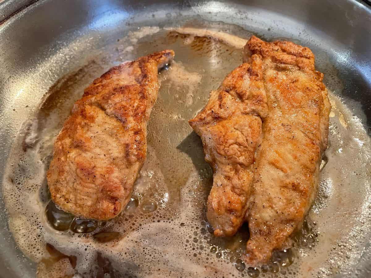 two chicken breast cooking in butter/oil in stainless steel skillet