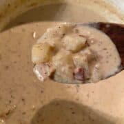 wooden spoon full of clam chowder over dutch oven of chowder