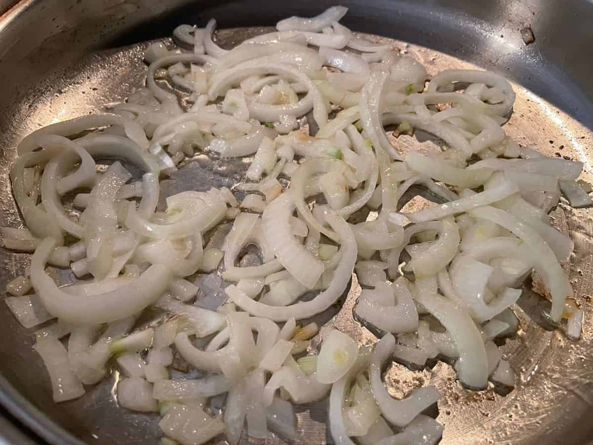 slices of onion cooking in a stainless steel skillet