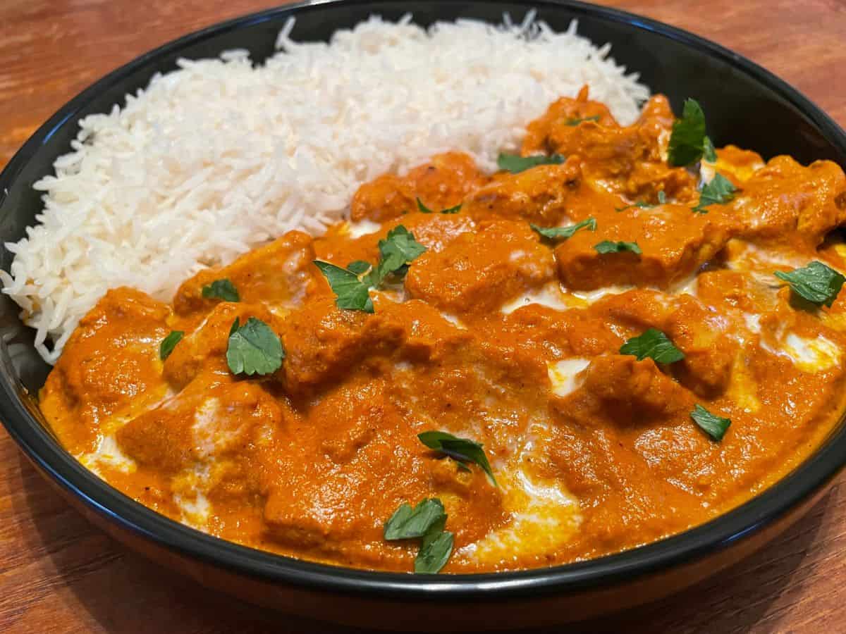 close up of butter chicken served with basmati rice in a black dinner bowl